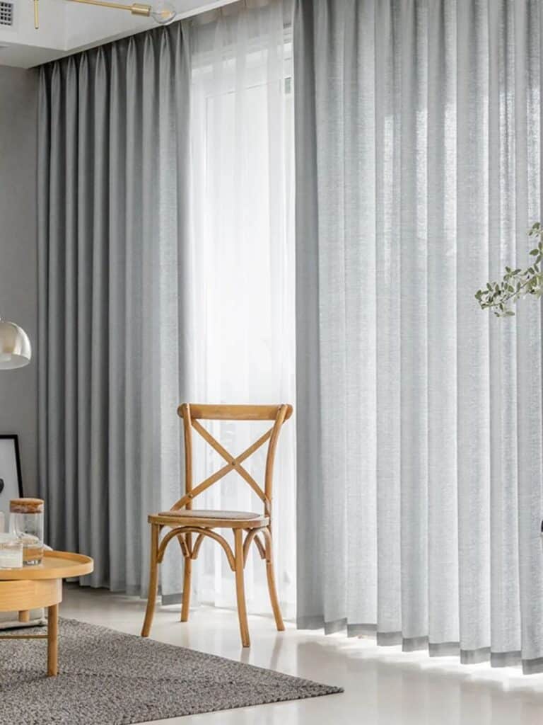Grey curtains over white sheer curtain in living area with chair placed in front of it
